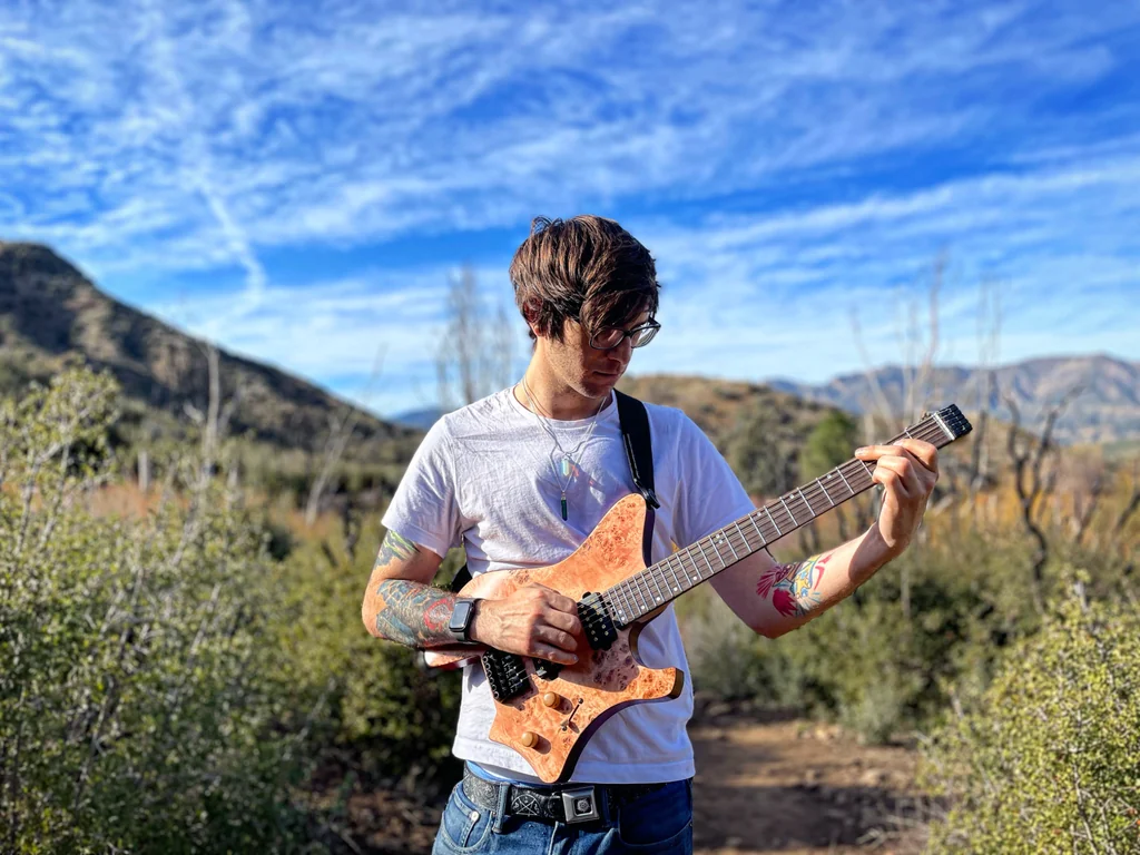 Kevin Cogen playing an electric guitar outdoors in a mountain landscape
