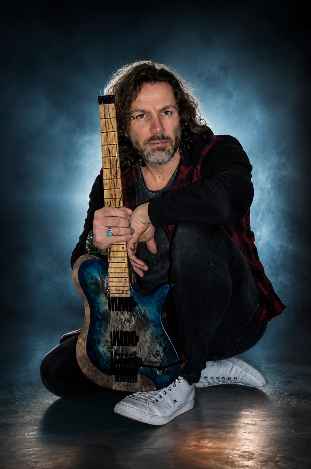 PineGap guitarist holding a blue electric guitar in a dramatic studio portrait