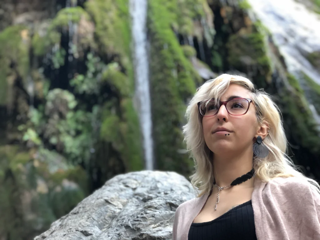 Pixienightmare standing in front of a green waterfall landscape
