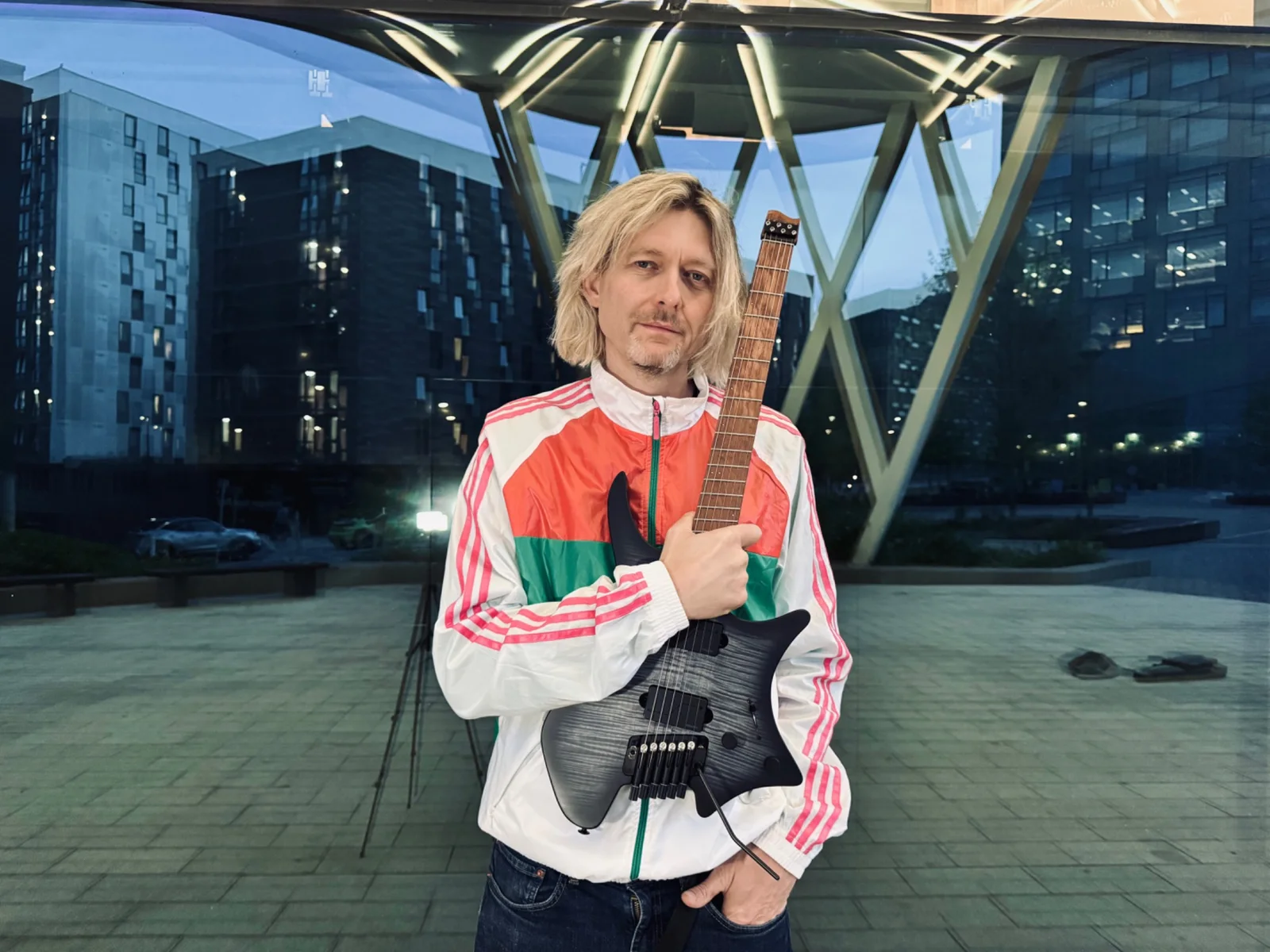 Tim Hutch holding a Strandberg guitar in a modern architectural setting